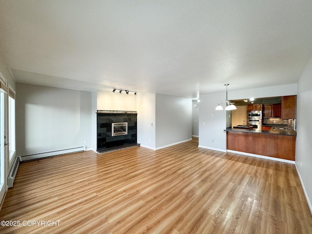 unfurnished living room featuring a textured ceiling, light wood-type flooring, baseboard heating, and sink