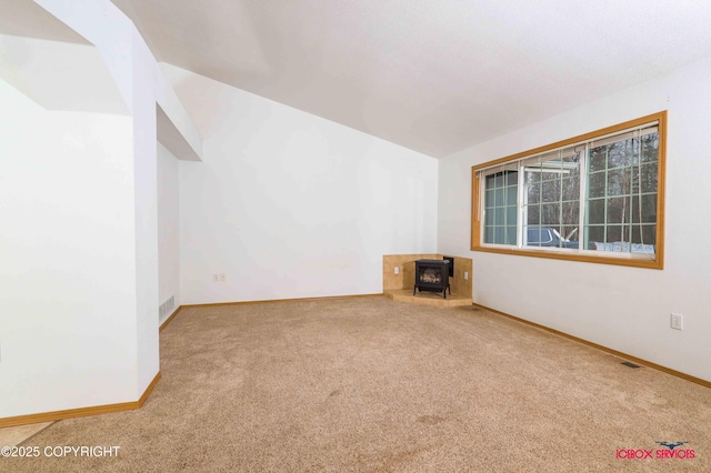 carpeted empty room with a wood stove and vaulted ceiling