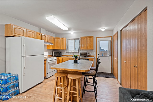 kitchen with a kitchen bar, a center island, light hardwood / wood-style floors, and white appliances