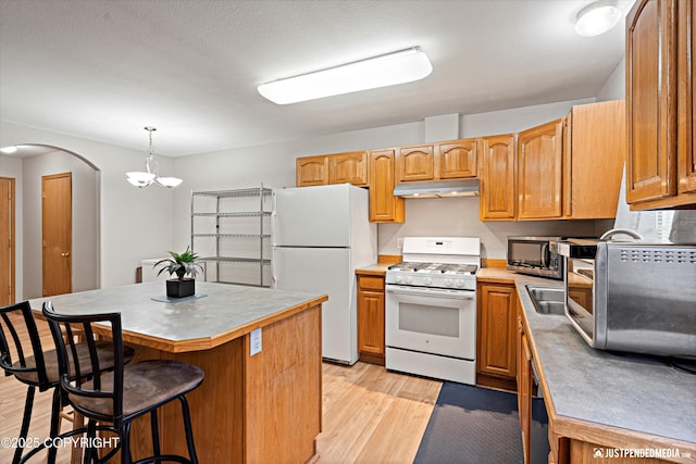 kitchen featuring a center island, a chandelier, decorative light fixtures, white appliances, and light hardwood / wood-style floors