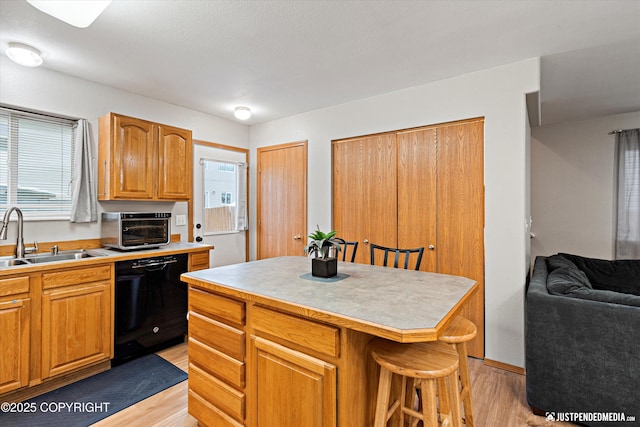 kitchen with sink, a center island, black dishwasher, a breakfast bar area, and light wood-type flooring