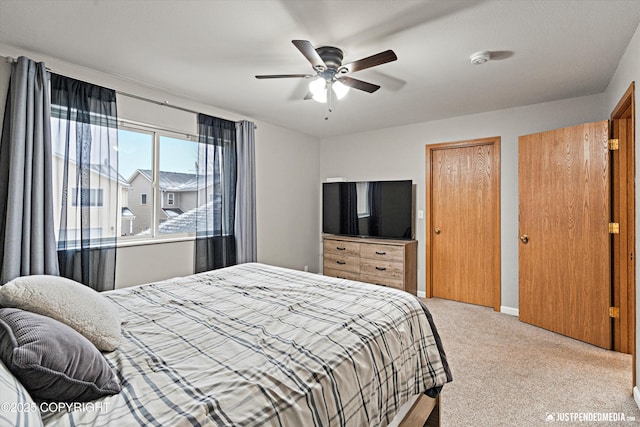 bedroom featuring ceiling fan, light colored carpet, and multiple closets