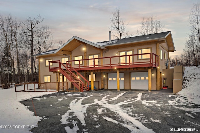 view of front facade featuring a wooden deck, stairs, stucco siding, a garage, and driveway