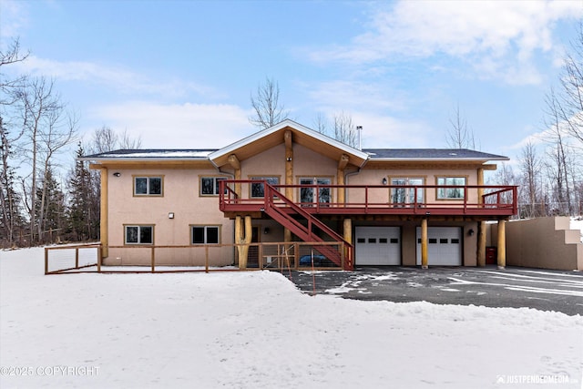 snow covered property featuring stucco siding, a deck, an attached garage, and stairway