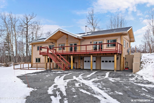 view of front of property with aphalt driveway, a wooden deck, stairs, stucco siding, and a garage