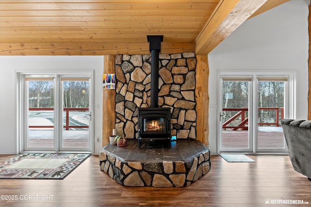 living room featuring beam ceiling, a wood stove, wood finished floors, and a healthy amount of sunlight