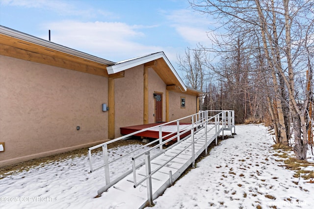 view of snow covered exterior featuring stucco siding and stairway