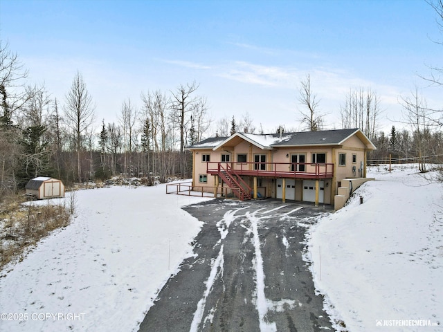 snow covered rear of property with stairway, an outdoor structure, a storage unit, a garage, and a deck