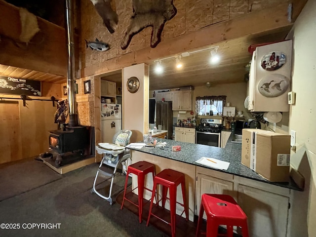 kitchen featuring a wood stove, track lighting, a kitchen breakfast bar, stainless steel stove, and white fridge