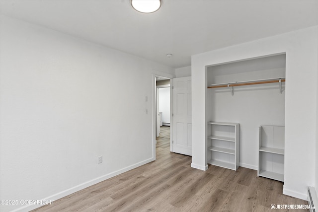 unfurnished bedroom with baseboard heating, a closet, and light wood-type flooring