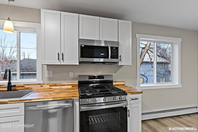 kitchen with wood counters, white cabinetry, sink, baseboard heating, and stainless steel appliances