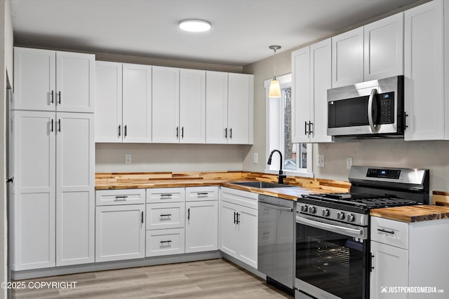 kitchen with wood counters, decorative light fixtures, stainless steel appliances, and white cabinets