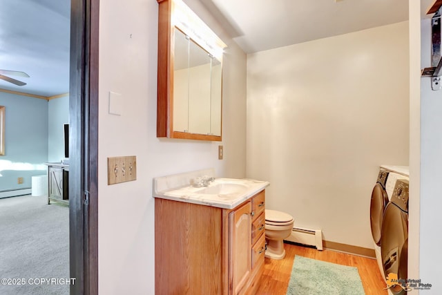 bathroom featuring independent washer and dryer, ceiling fan, toilet, a baseboard heating unit, and vanity