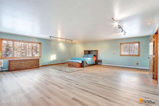 unfurnished bedroom with rail lighting, baseboard heating, and light hardwood / wood-style floors