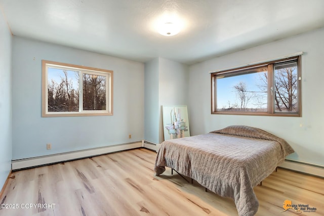 bedroom featuring a baseboard heating unit, light hardwood / wood-style flooring, and multiple windows