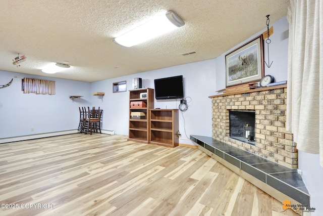 interior space featuring a textured ceiling, baseboard heating, a tiled fireplace, and hardwood / wood-style flooring