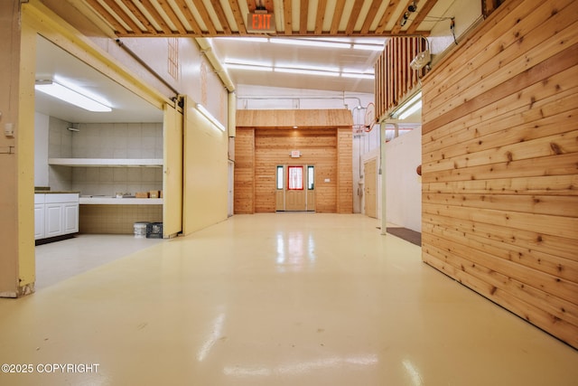 hallway with wood walls, a towering ceiling, and concrete floors