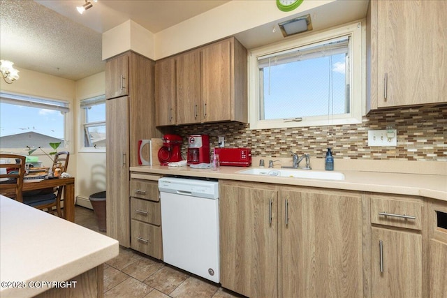 kitchen with backsplash, white dishwasher, sink, light tile patterned floors, and a textured ceiling