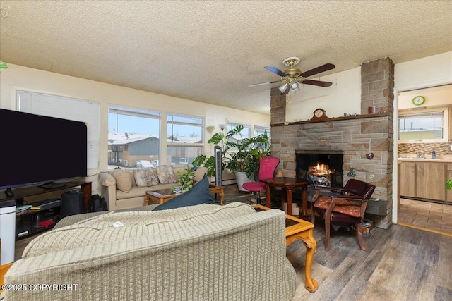 living room featuring a stone fireplace, ceiling fan, dark hardwood / wood-style floors, and a textured ceiling