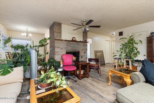 living room with a textured ceiling, ceiling fan with notable chandelier, light hardwood / wood-style floors, and a stone fireplace