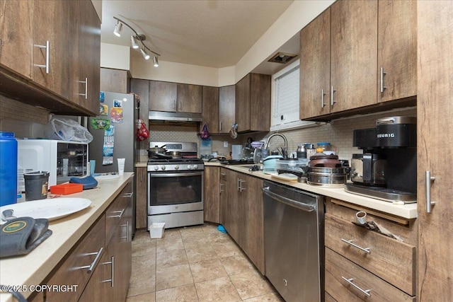 kitchen featuring dark brown cabinetry, sink, stainless steel appliances, backsplash, and light tile patterned flooring