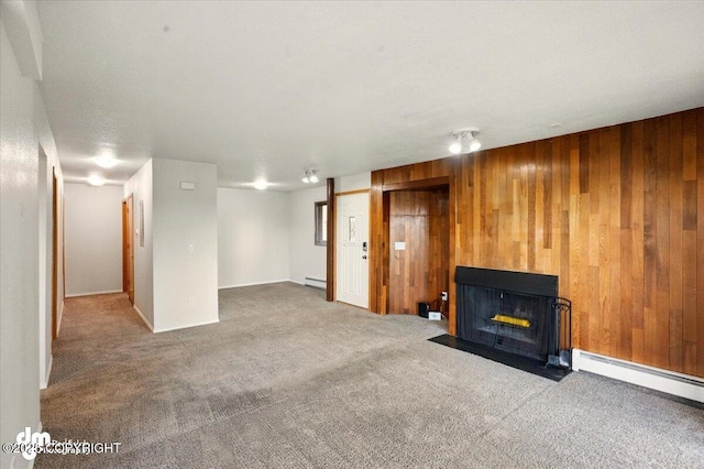 unfurnished living room featuring carpet, wood walls, a fireplace with flush hearth, and baseboard heating