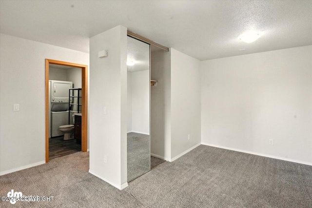 unfurnished bedroom with stacked washer and clothes dryer, carpet floors, a closet, baseboards, and a textured ceiling