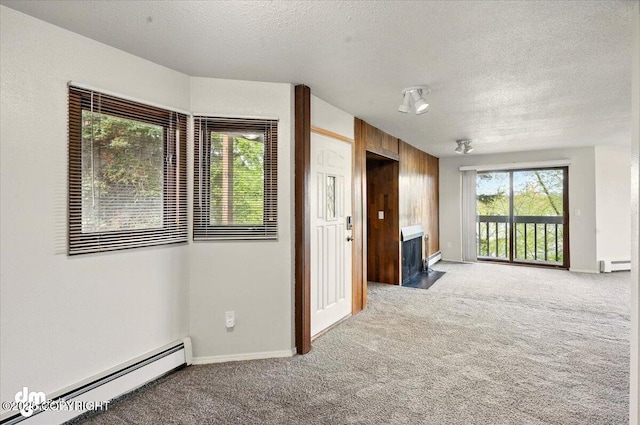 unfurnished room with baseboard heating, a baseboard heating unit, light colored carpet, a textured ceiling, and a fireplace with flush hearth