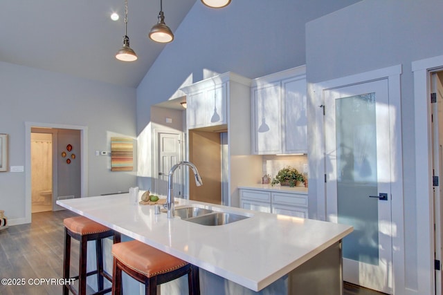 kitchen with pendant lighting, lofted ceiling, a kitchen island with sink, white cabinets, and sink