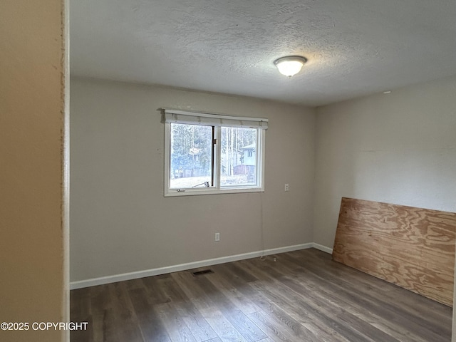 empty room with visible vents, a textured ceiling, baseboards, and wood finished floors