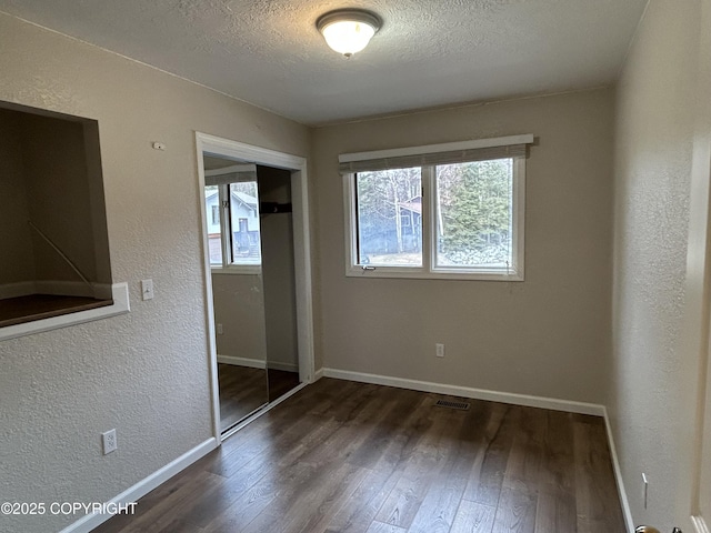 unfurnished bedroom with a closet, a textured ceiling, baseboards, and wood finished floors