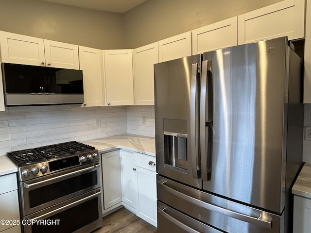 kitchen with dark wood-type flooring, white cabinets, appliances with stainless steel finishes, backsplash, and light stone countertops