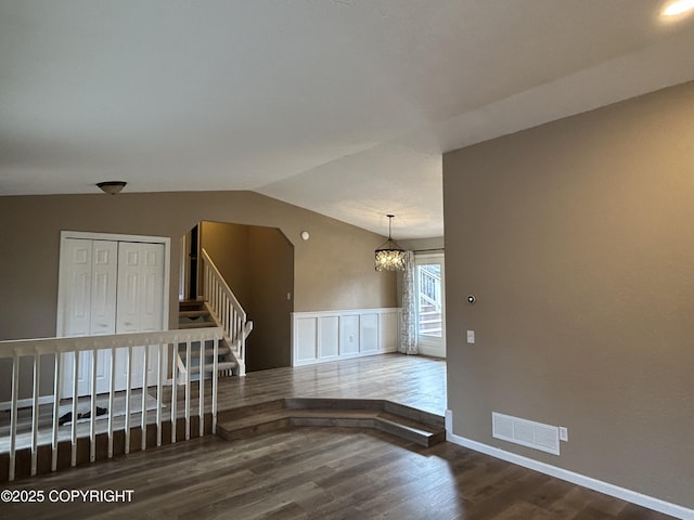 unfurnished room featuring wood finished floors, visible vents, stairs, vaulted ceiling, and wainscoting