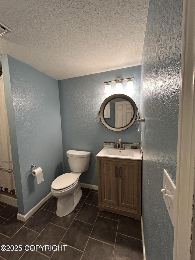 bathroom featuring baseboards, a textured wall, toilet, a textured ceiling, and vanity