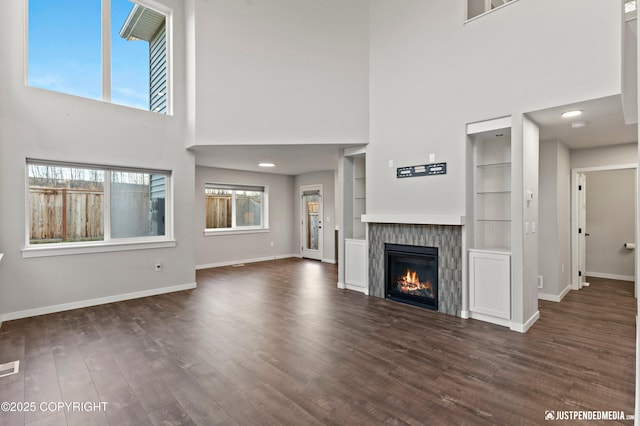 unfurnished living room with built in shelves, dark hardwood / wood-style floors, and a high ceiling