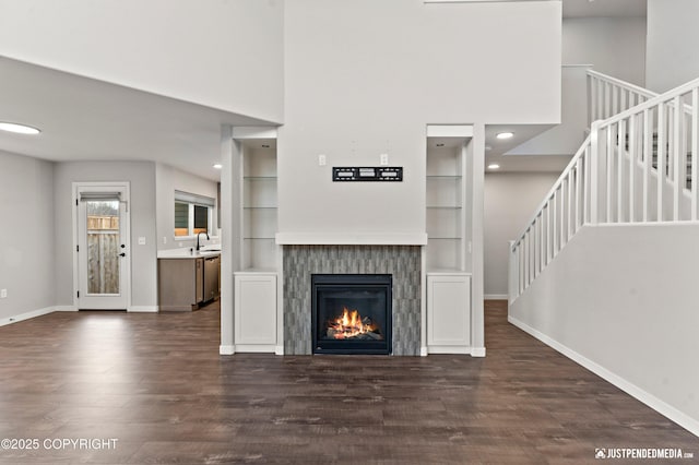 unfurnished living room with dark wood-type flooring, built in features, sink, and a fireplace