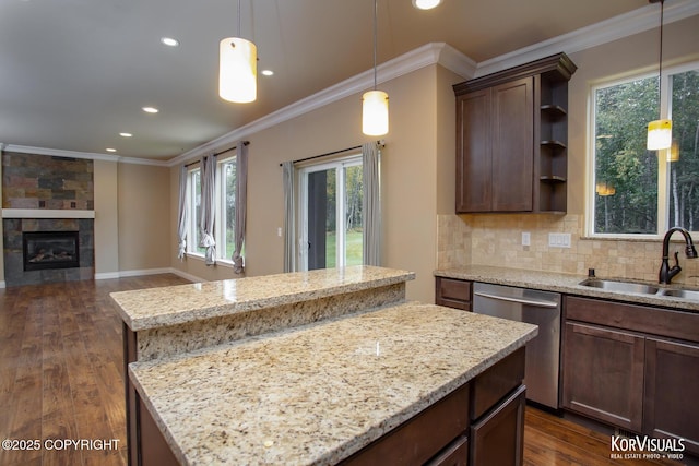 kitchen featuring dishwasher, sink, light stone countertops, a kitchen island, and a tiled fireplace