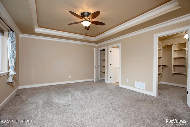 unfurnished bedroom featuring ornamental molding, a raised ceiling, ceiling fan, a spacious closet, and a closet