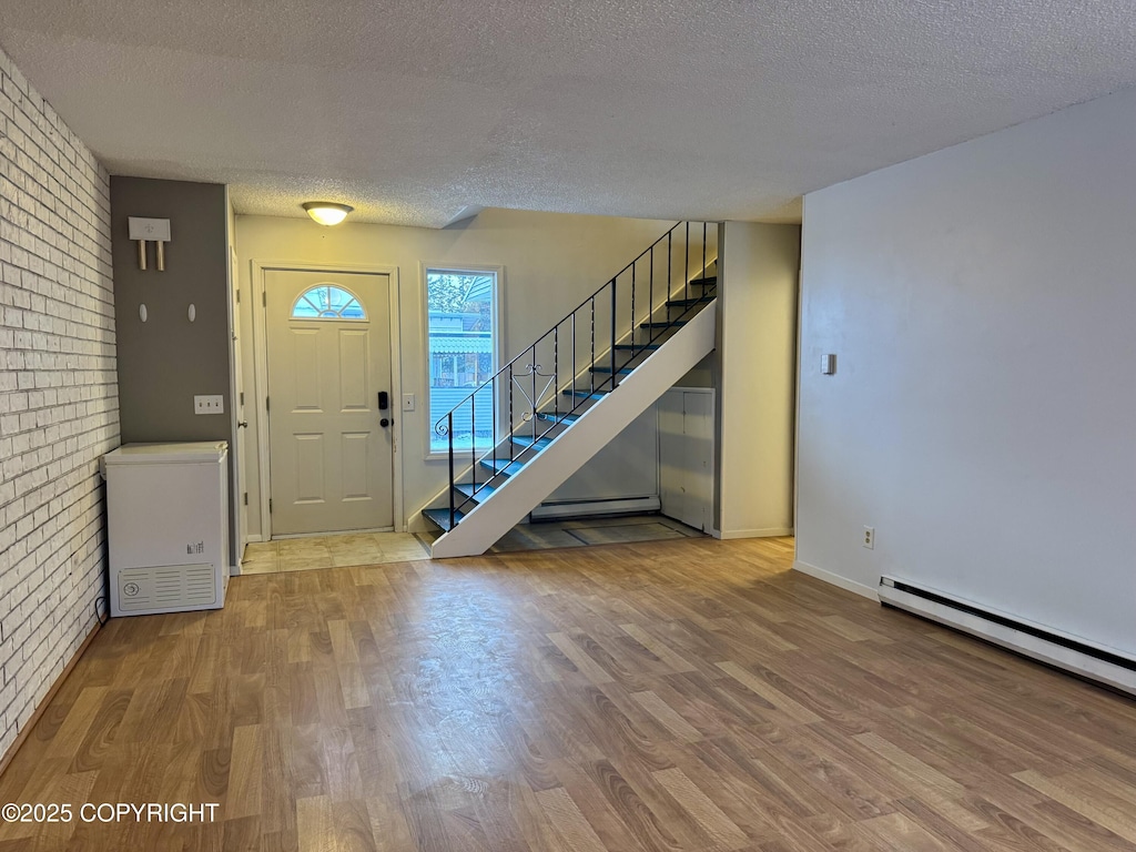 entryway with baseboard heating, brick wall, a textured ceiling, and light hardwood / wood-style floors