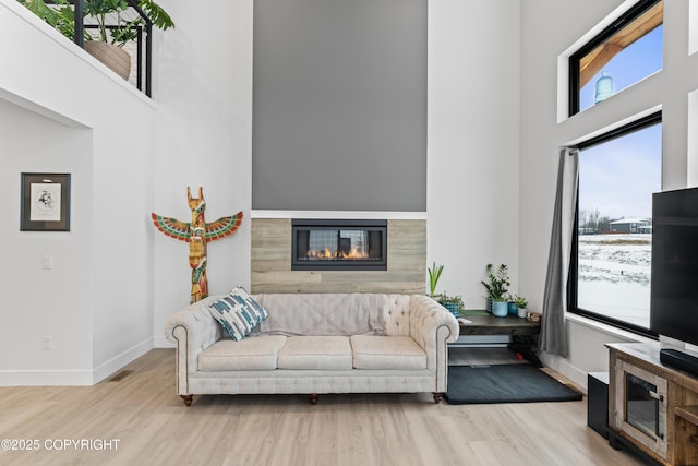 living room with light hardwood / wood-style floors, a fireplace, and a high ceiling