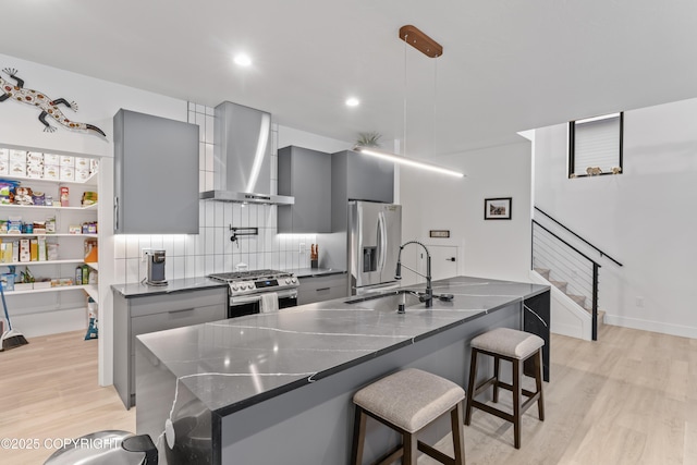 kitchen with gray cabinetry, a breakfast bar, pendant lighting, wall chimney range hood, and stainless steel appliances