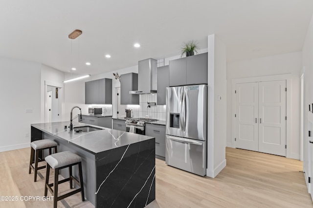 kitchen with wall chimney exhaust hood, stainless steel appliances, a breakfast bar area, gray cabinets, and a kitchen island