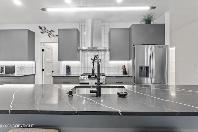 kitchen with appliances with stainless steel finishes, dark stone countertops, gray cabinetry, and wall chimney range hood