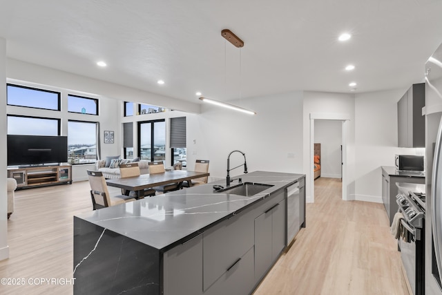 kitchen featuring light wood-type flooring, stainless steel appliances, sink, decorative light fixtures, and a large island