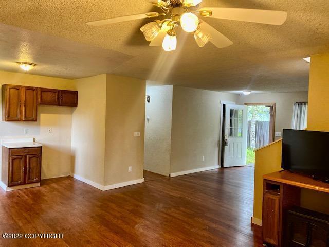 unfurnished living room with ceiling fan, dark hardwood / wood-style flooring, and a textured ceiling