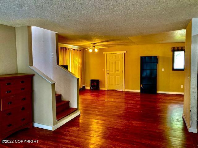 unfurnished living room featuring a textured ceiling, dark hardwood / wood-style flooring, and ceiling fan