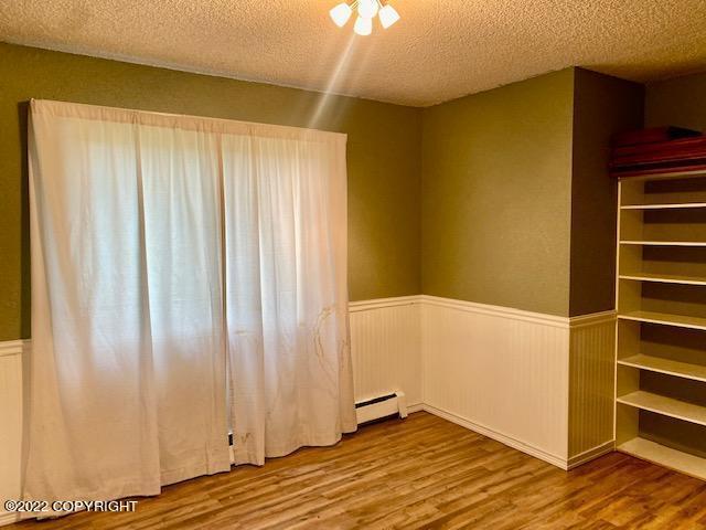 unfurnished room with a textured ceiling, baseboard heating, and hardwood / wood-style flooring