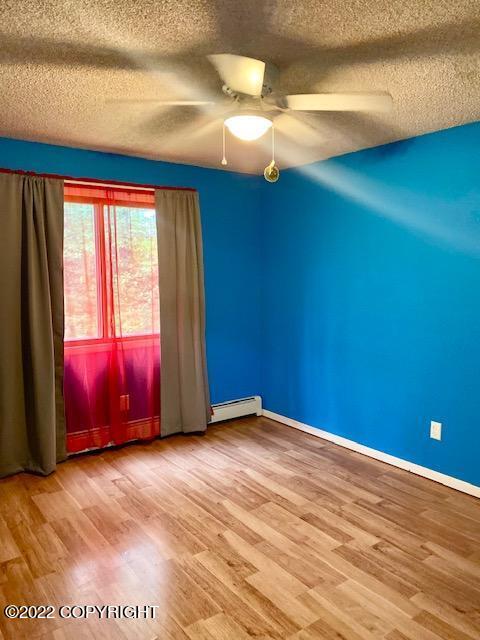 spare room with a textured ceiling, hardwood / wood-style flooring, ceiling fan, and a baseboard heating unit