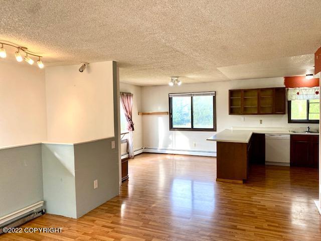 kitchen with dark brown cabinetry, dishwasher, a baseboard radiator, and hardwood / wood-style flooring