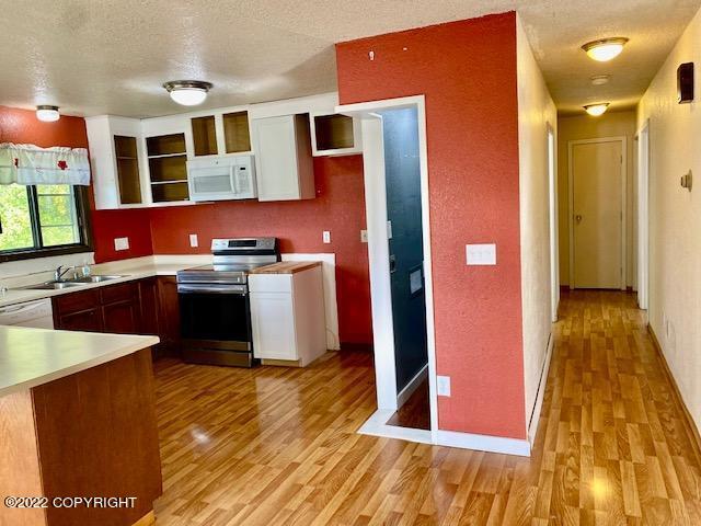 kitchen with a textured ceiling, light hardwood / wood-style flooring, white appliances, and sink